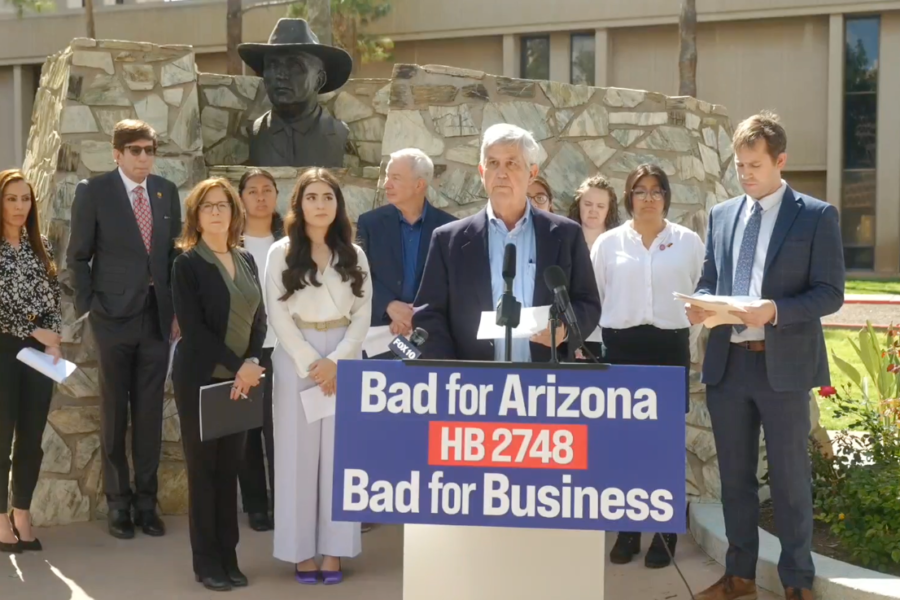 This image shows a group of diverse individuals standing behind a podium with a sign that reads 'Bad for Arizona HB 2748 Bad for Business' prominently displayed.